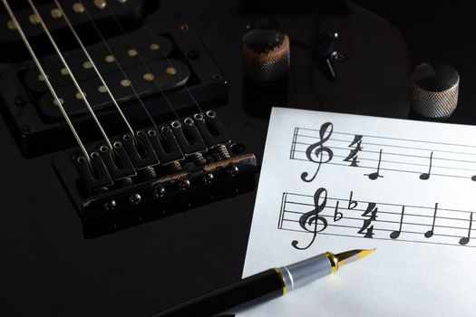 Music note and vintage pen on black electric guitar in darkness. Concept of rock music creative.