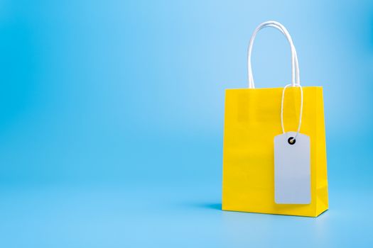 Single yellow gift or shopping bag with blank label tag isolated on blue background