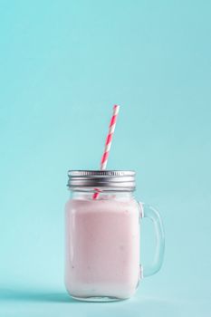 Pink strawberry smoothie in mason jar glass. Isolated on blue background. Vertical.