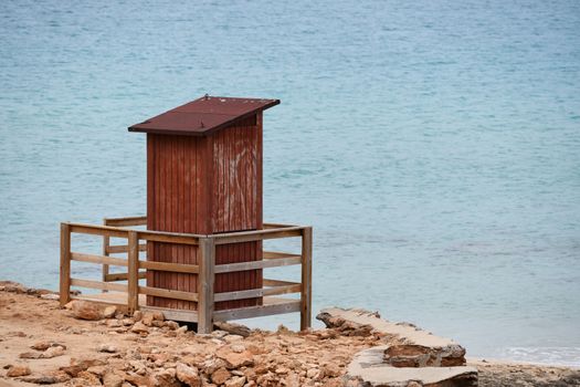 A brown wooden lifeguard house in an empty beach with clear blue sea in Ibiza