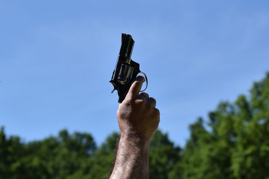 A man pointing to a clear blue sky with a gun before starting an athletes race with background green trees