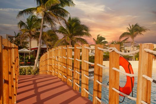 A walking bridge across a tropical resort swimming pool in warm light