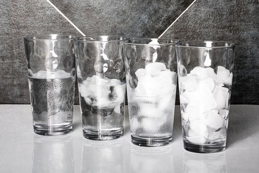 View of four glasses of ice on a table top, each at a different stage of melting.
