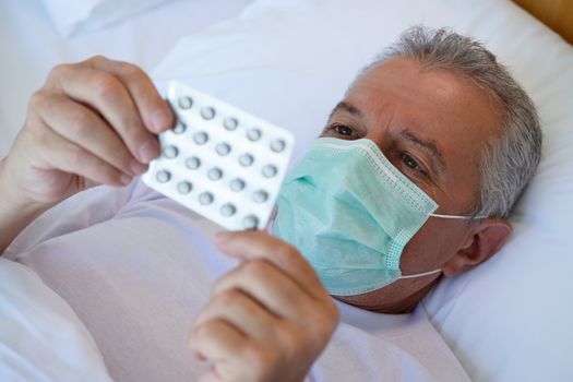 Selective focus closeup. Cropped image of Sick man in bed bed with medical face mask, taking medicines and drugs. Treatment, fever or  flu virus concept. 