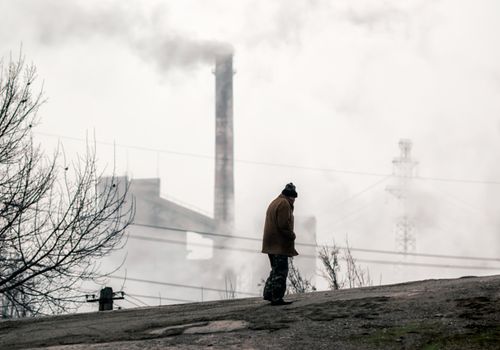 lonely beggar man on the background of smoking chimneys of a factory in Donbass Ukraine