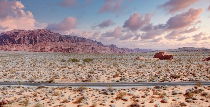 A two lane highway across the desert with rocks in distance