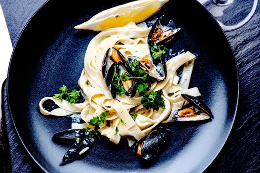 Blue mussels and pasta in black plate on stone surface