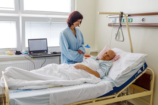 Woman without hair after chemotherapy patient lying at hospital bed feeling sad and depressed worried. A friend came to please her. Health care and clinical attention concept.