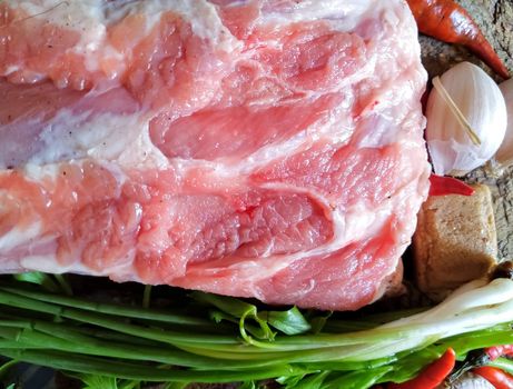 Fresh pork and vegetables placed on a wooden chopping board, ready for cooking