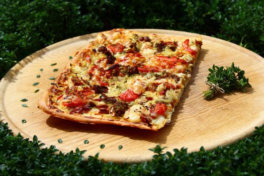 The picture shows a piece of pizza on a wooden board in a thyme field