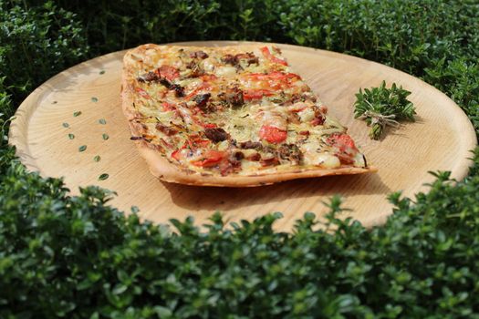 The picture shows a piece of pizza on a wooden board in a thyme field