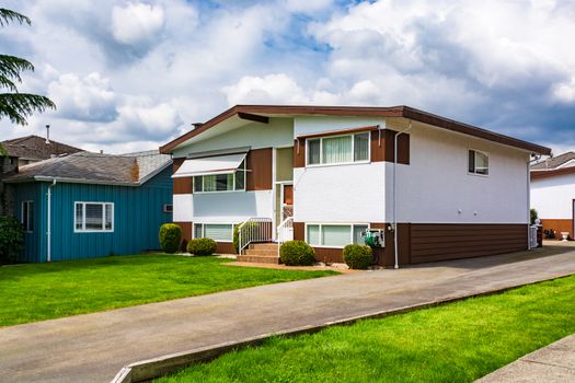 Family house with green lawn in front. Average residential house on cloudy day in British Columbia