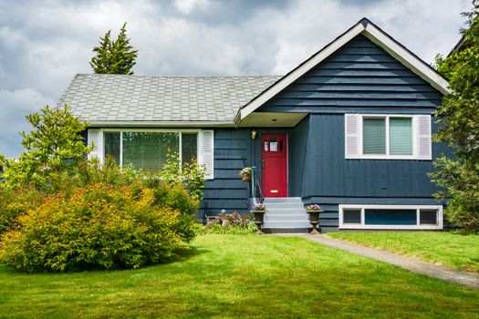 Small family house with green lawn and decorative flowers at the entrance. Average residential house on sunny day in British Columbia