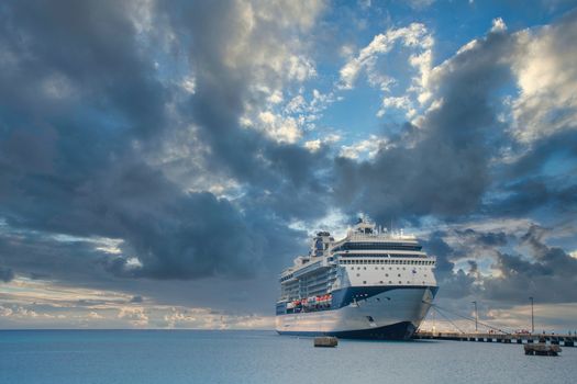 A massive luxury blue and white cruise ship at a dock in the tropics under a storm cloud