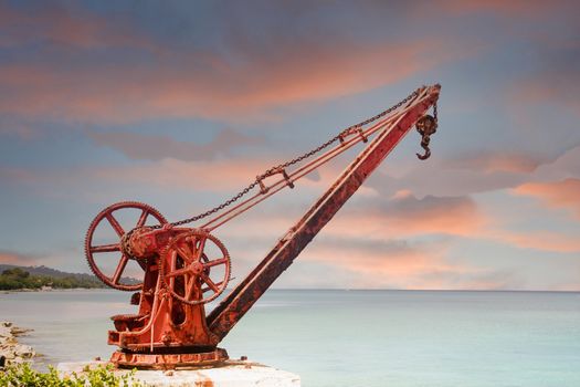 An old rusty, red crane with manual crank on the shore of a tropical island