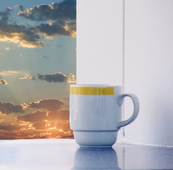 A white porcelain coffee cup sitting on a table on a sunny patio at sunrise