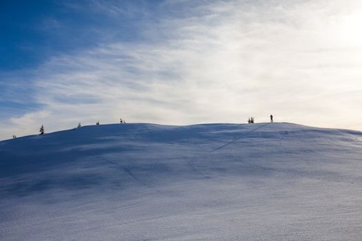 Hiker  with long shadow on top of Mount Ciucas peak on a sunny winter day at sunset, part of Romanian Carpathian Range