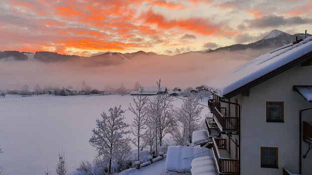 Sunrise over Snowy Mountains With German looking Building against a red and Yellow Sky