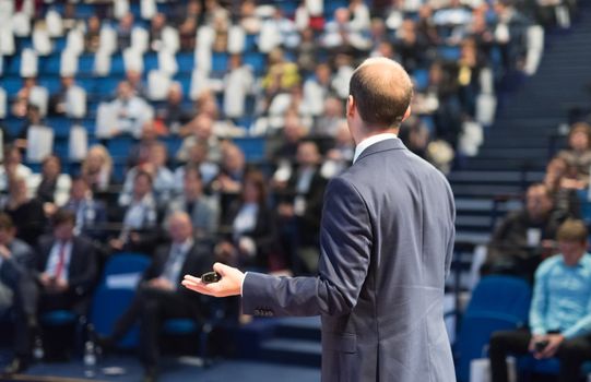 Rear view of speaker giving a talk on corporate business conference. Unrecognizable people in audience at conference hall. Business and Entrepreneurship event.