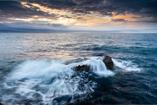 Portmuck, Islandmagee, County Antrim, Northern Ireland:  under a dramatic sunset sky, waves break over rocks close to the shore.