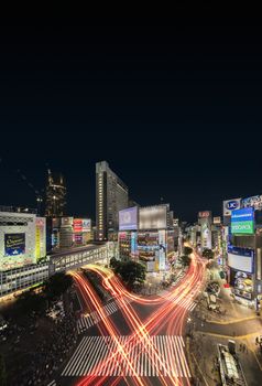 Aerial view of the Shibuya Crossing Intersection in front of Shibuya Station on a summer night with the speed lights flow of cars.