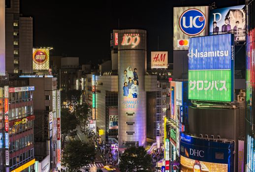 Aerial view of the Shibuya Crossing Intersection in front of Shibuya Station on a summer night with the speed lights flow of cars.