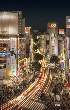 Aerial view of the Shibuya Crossing Intersection aera in front of Shibuya Station on a summer night with the speed lights flow of cars.