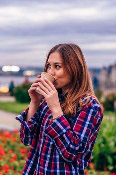 Coffee on the go. Beautiful young woman drinking coffee in the park