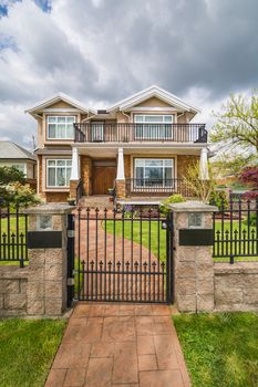 Luxury residential house with green lawn on the front yard behind metal fence