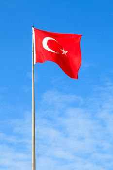 A Turkish flag flying from a flag pole on a beautiful sunny day.