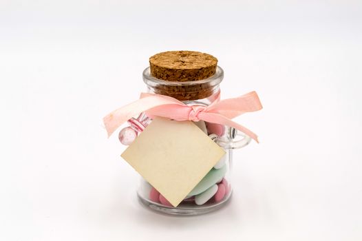 Colorful sweet almonds in a glass container with a pacifier and a cork for a baptism, on a white background