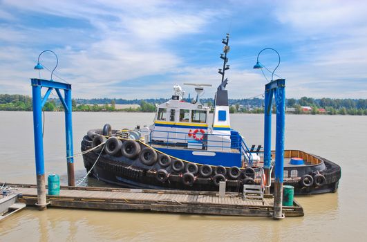 Small tugboat moored at river pier on blue sky background