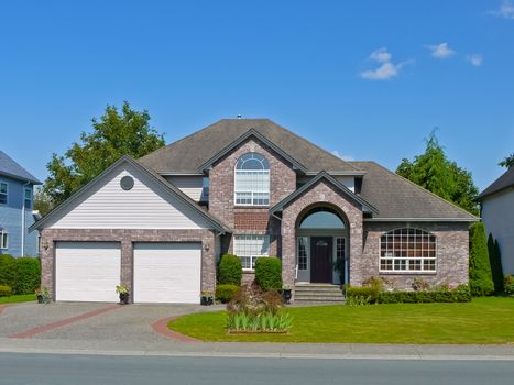 Large residential house with double garage and concrete driveway on blue sky background