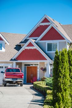 Entrance of luxury residential house with red truck parked on the driveway. Red residential house with red car in front of the entrance