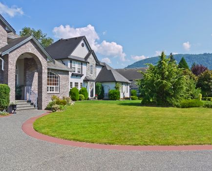 Rounded driveway and lawn in front of residential houses on blue sky background. Luxury family houses with landscaped front yards and mountains view