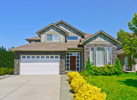 Luxury family house with concrete driveway to the garage on blue sky background. Yellow flowers way