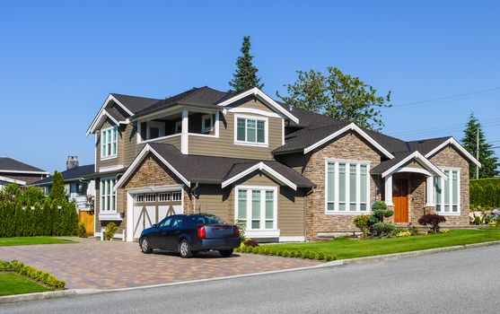 Luxury residential house with green hedge and green lawn. Suburban family house with double garage and car parked on paved driveway