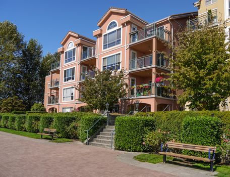 Apartement building in residential area on sunny day. Condo building with bench and walkway in front