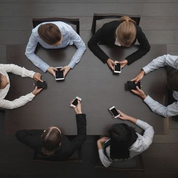 Business people with blank phone sitting around the table, top view