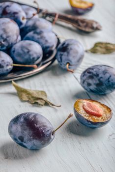 Ripe plums with sliced fruits, leaves and vintage knife over light wooden surface