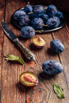 Ripe plums on wooden table with leaves and vintage knife