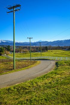Country road leading to a cattle farm on winter season. Asphalt road to a valley in British Columbia. Rural road with power posts on the side and mountain view background