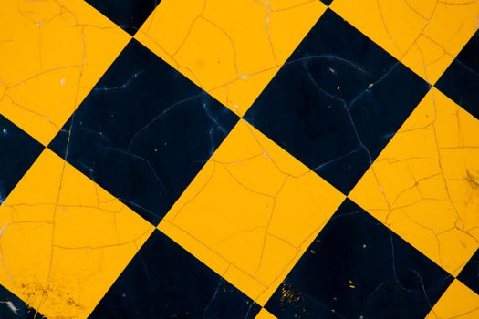 A metal sign marking the end of a road has a black-and-yellow pattern of diamonds. Cracks in its painted surface can be seen.