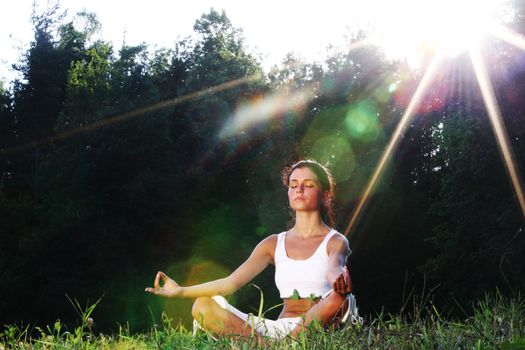 Young yoga woman on green grass lotus pose in sunrise light