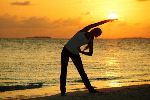Yoga woman silhouette over sunset sky and sea background