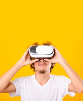 Asian handsome man with curly hair he using virtual reality headset or VR glass isolate on yellow background