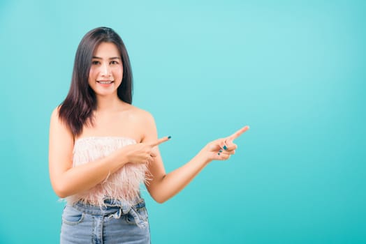 Portrait asian beautiful woman smiling looking camera her standing pointing finger out on blue background, with copy space for text