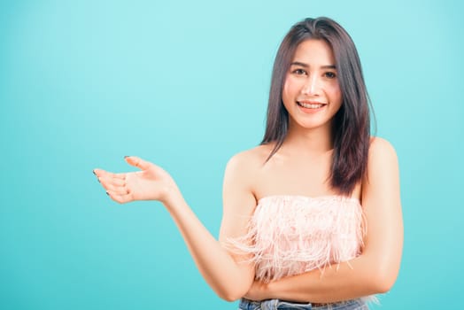 Smiling face Asian beautiful woman her showing hand something near body on blue background, with copy space for text