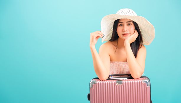 Portrait asian beautiful woman with hat her sitting with travel bag on weekends on blue background, with copy space for text