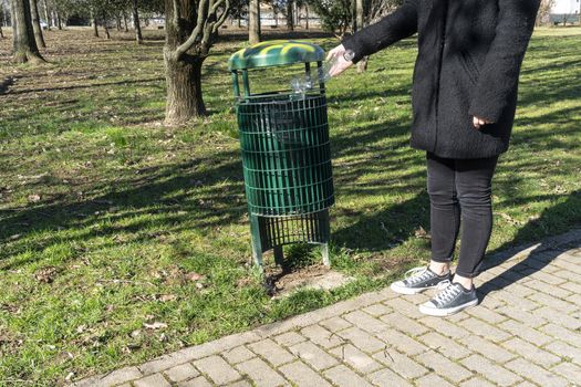 a girl picks up on the ground a plastic bottle and throws it in a waste basket